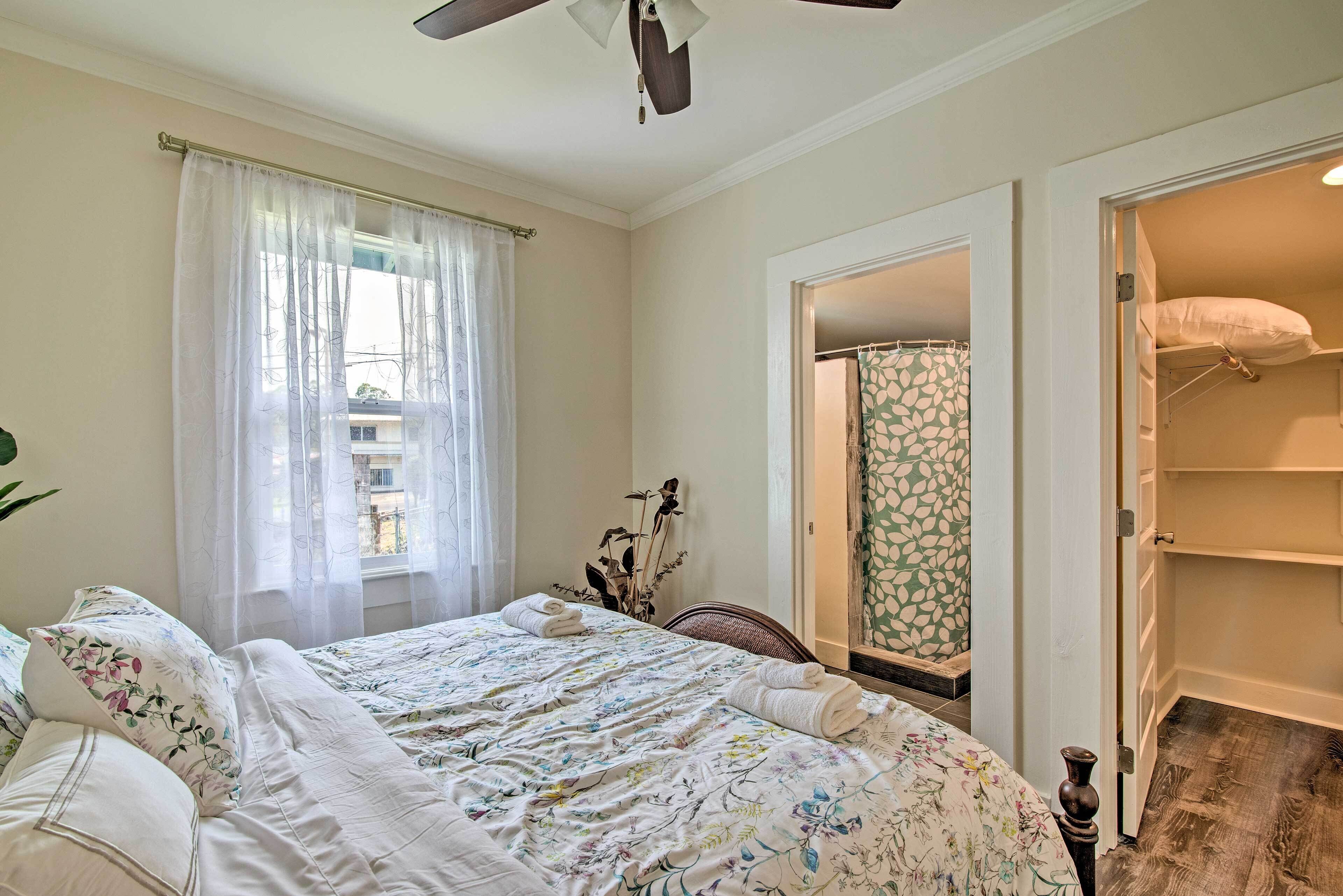 Un dormitorio con cama, ventana con cortinas ligeras, ventilador de techo y vestidor.