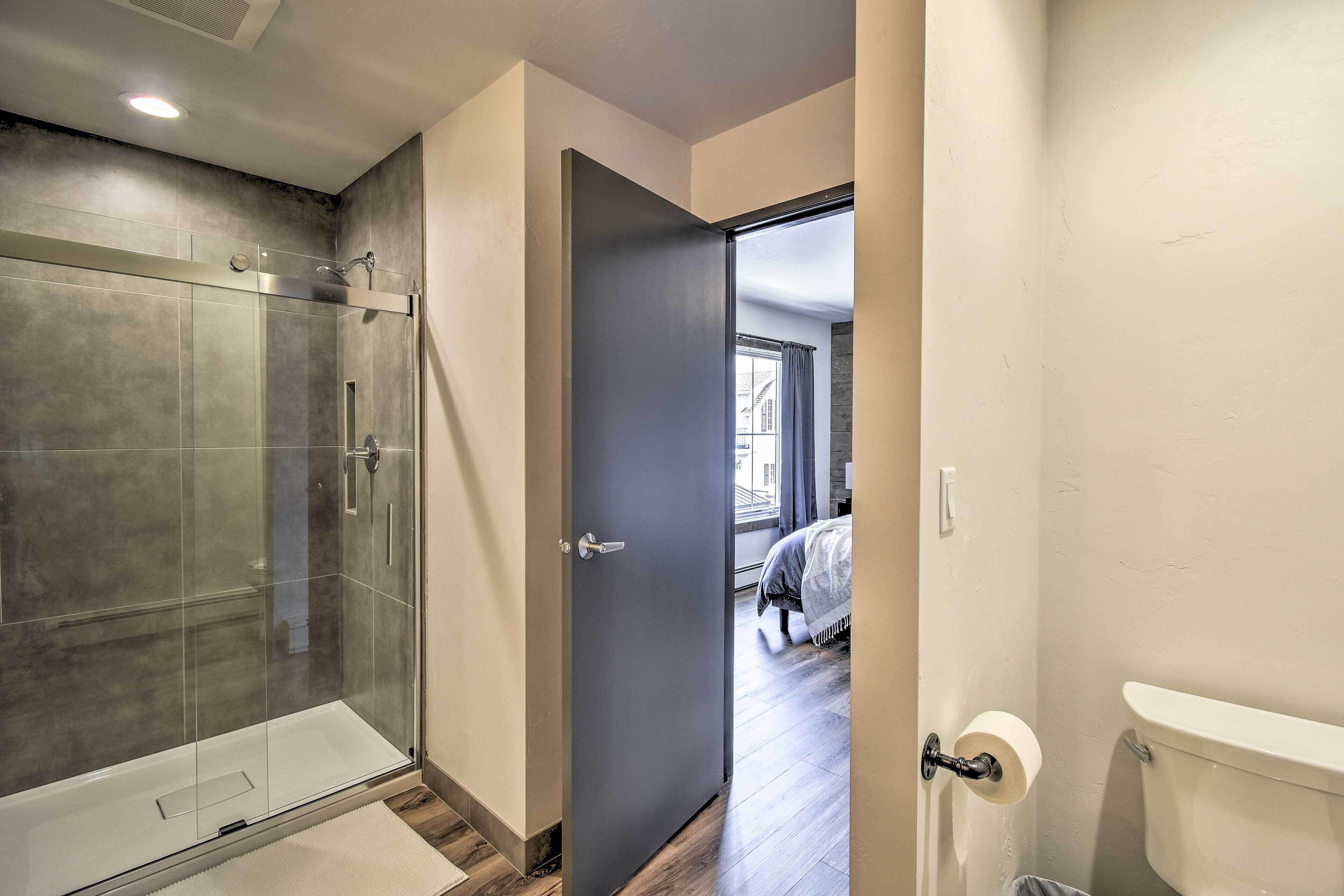 A modern bathroom with a glass shower enclosure, a toilet, and a door leading to a bedroom.