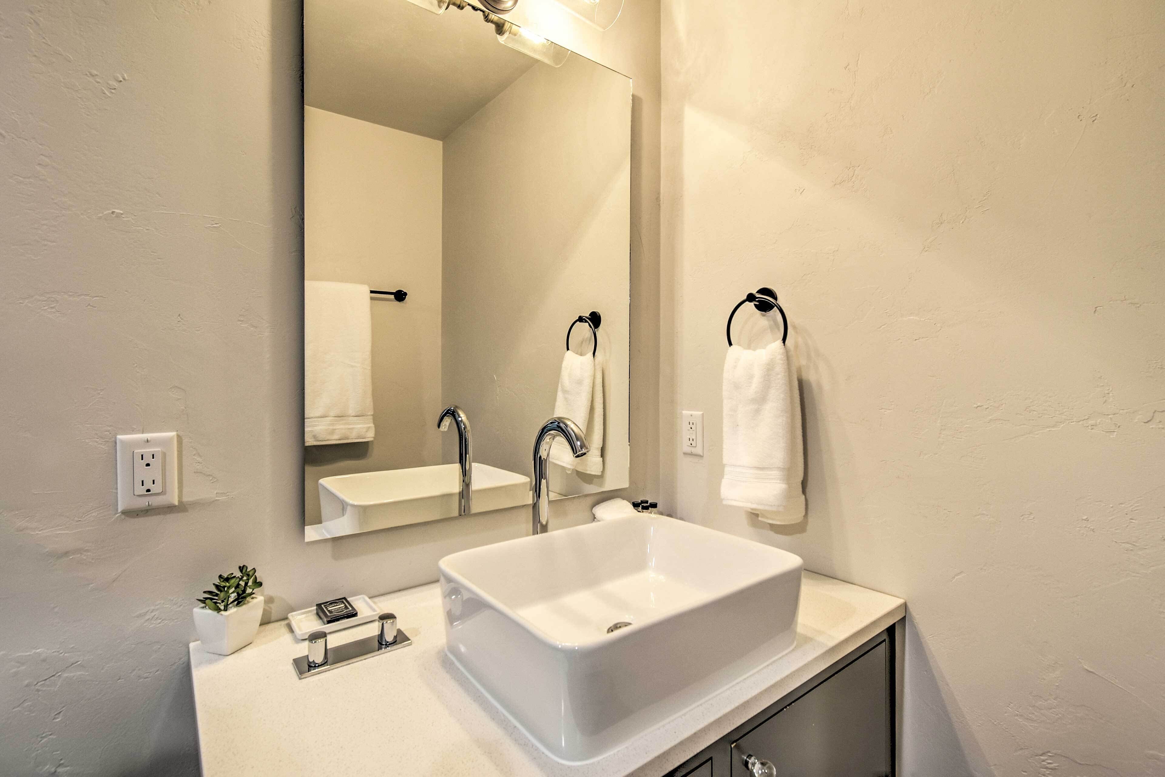 A modern bathroom with a large white sink, a mirror, and two towel hooks.