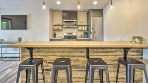 Uma cozinha moderna com ilha central, banquetas de bar e uma TV fixada na parede.
