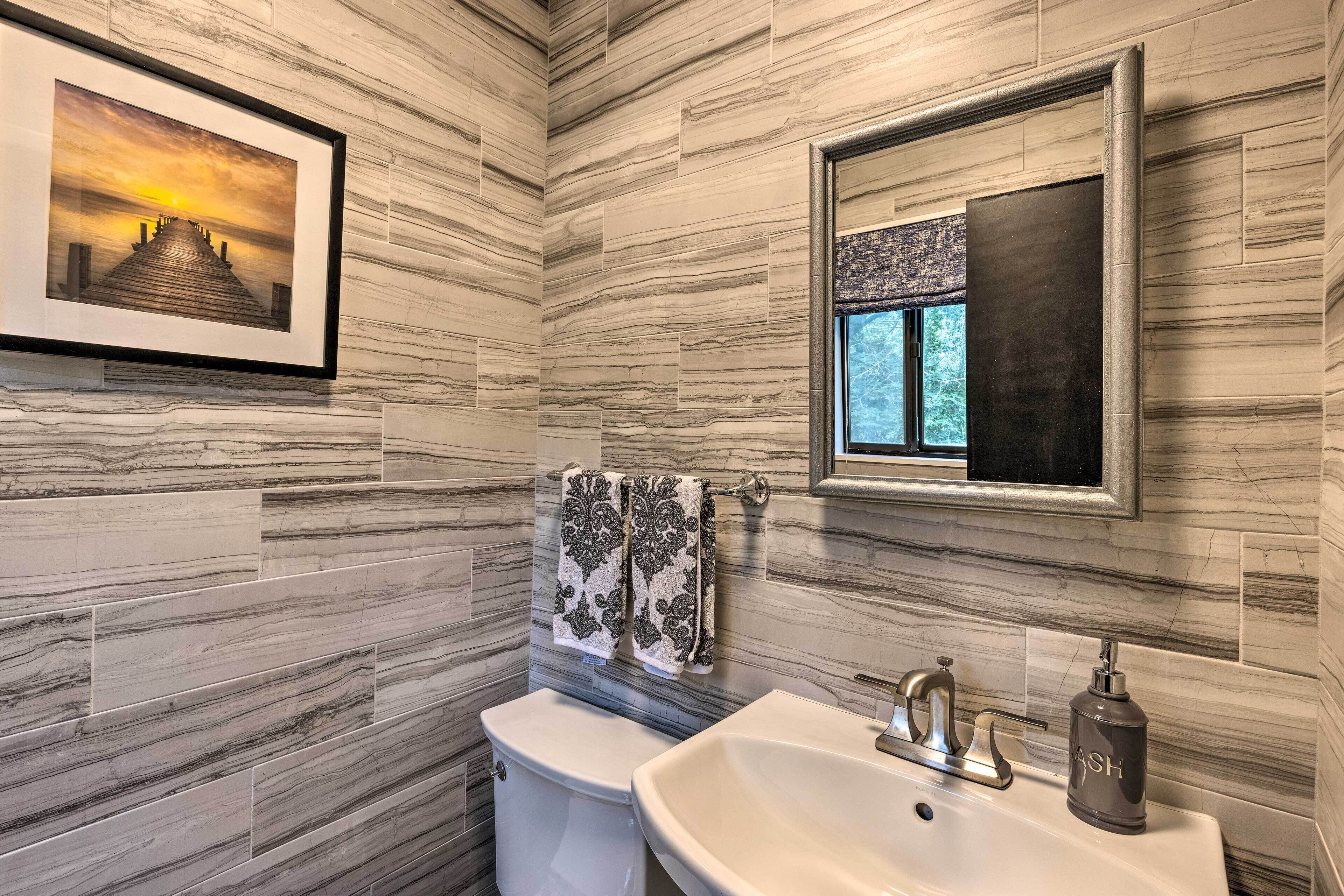 A bathroom with marble walls, a framed picture of a sunset, a sink with a soap dispenser, and a toilet.