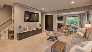 Un salon moderne avec un canapé, une table basse et un téléviseur. Un escalier se trouve à gauche, et un coin repas est aménagé avec une table et des chaises.