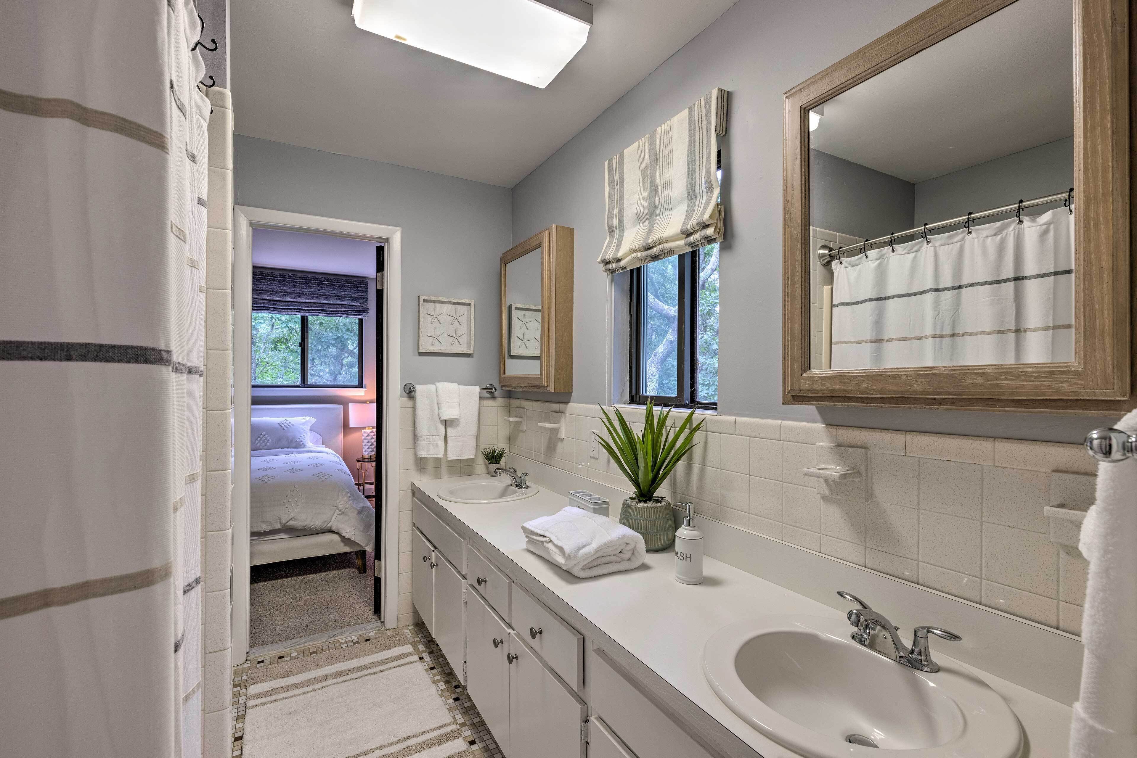 A modern bathroom with a double sink, large mirror, and a potted plant.