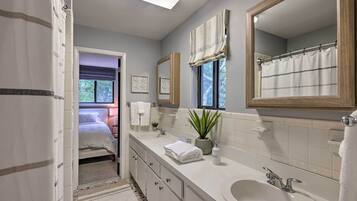 A modern bathroom with a double sink, large mirror, and a potted plant.