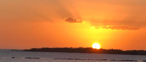 Un coucher de soleil sur une étendue d’eau calme, avec une côte visible au loin.