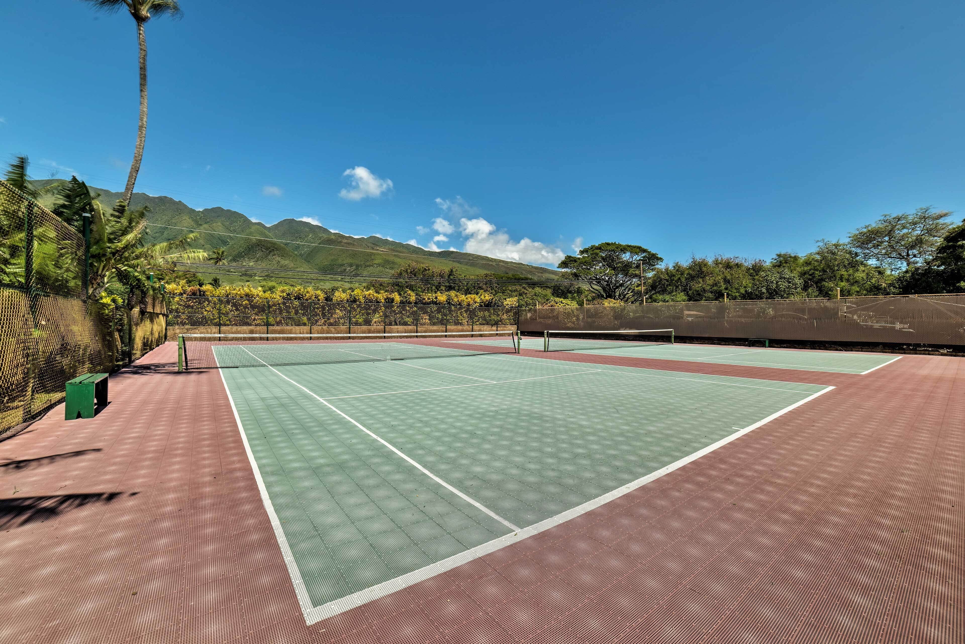 Una cancha de tenis con una red, rodeada por una valla, y una montaña al fondo.