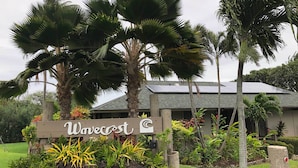 A sign with the name "Wavecrest" surrounded by tropical plants and palm trees. - High-end Resort Condo Nestled on Molokai Shoreline (Kaunakakai)