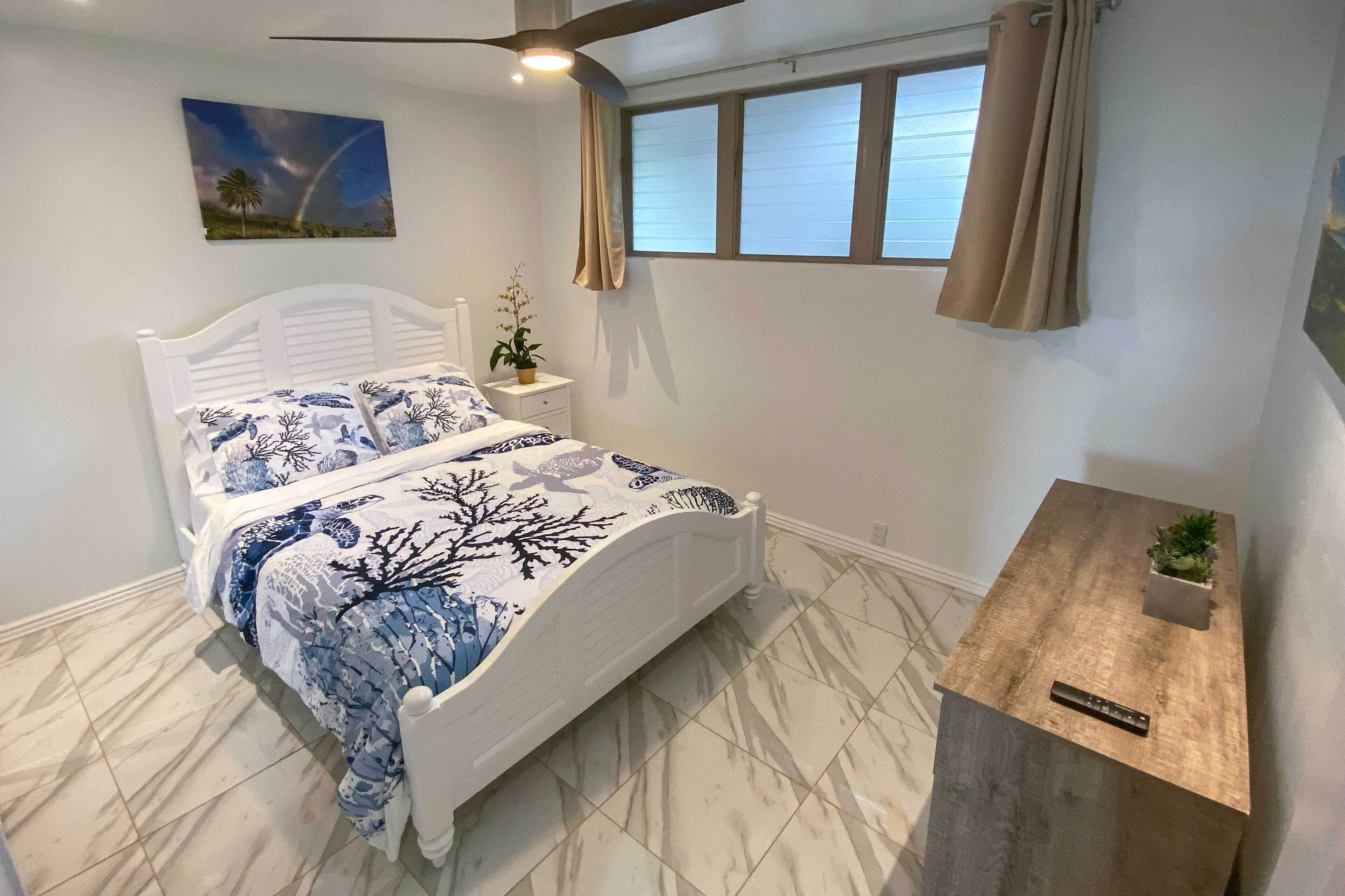 A bedroom with a bed, a nightstand, a small table with a plant, a window with curtains, and a painting on the wall.