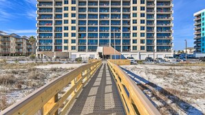 Ein mehrstöckiges Hotel mit zentralem Eingang, einem überdachten Gang und einem Strandabschnitt mit Sand.