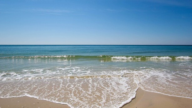 Ein Strand mit klarem, blauem Wasser und sanft anschwellenden Wellen.