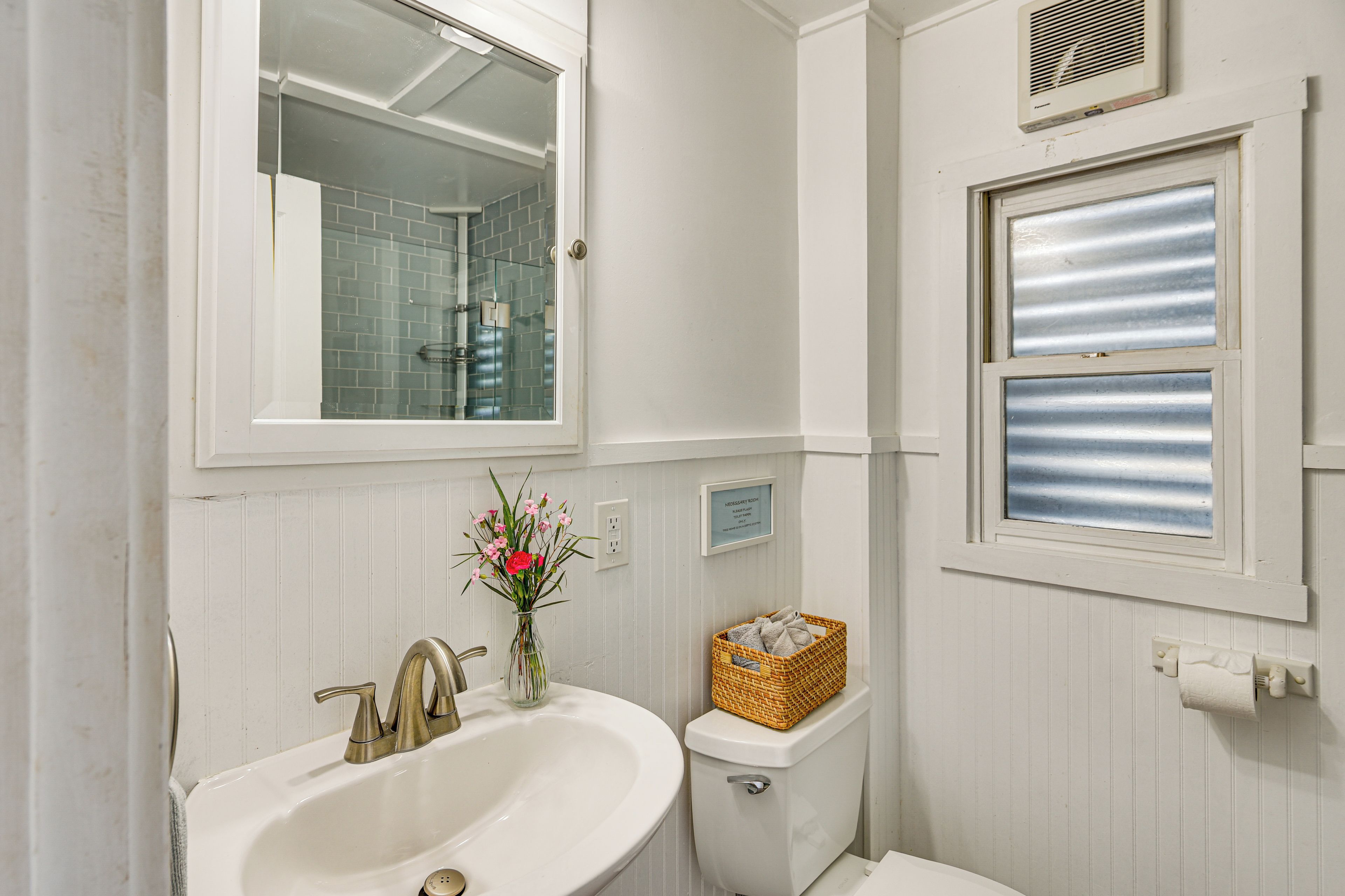 Une salle de bain avec un lavabo blanc, un miroir, des toilettes et une fenêtre.