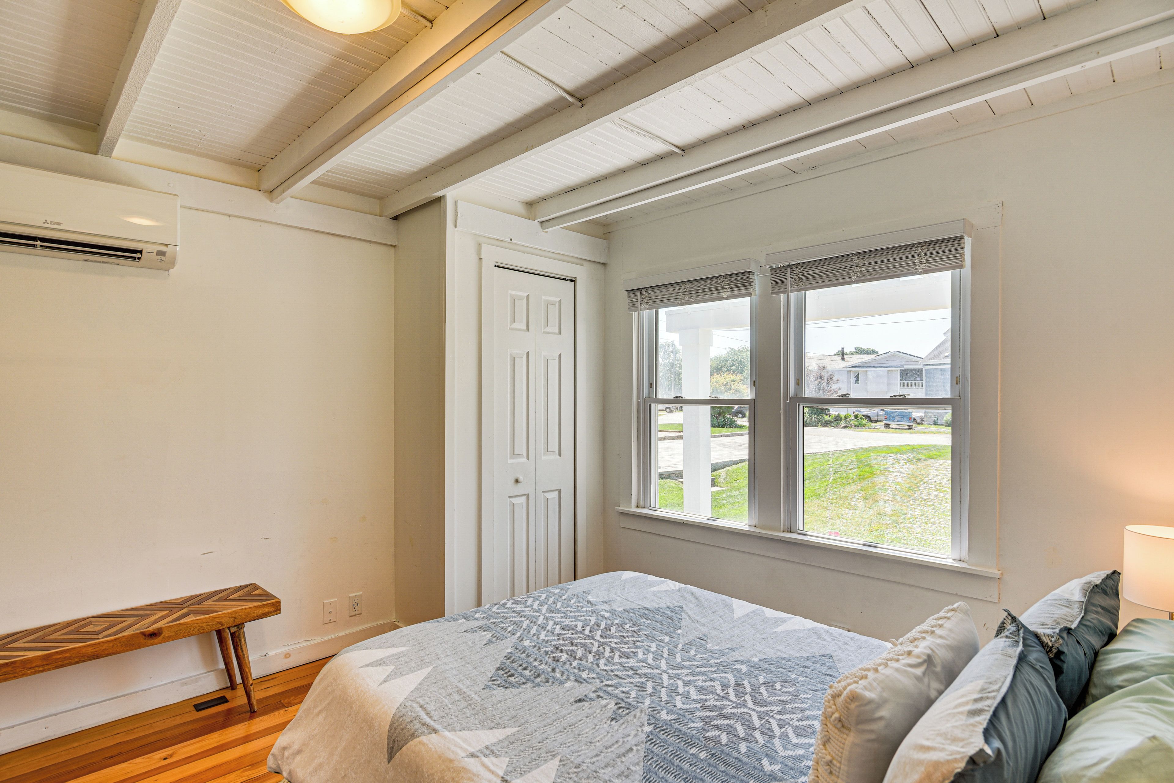 A bedroom with a bed, a bench, a window, and an air conditioning unit.