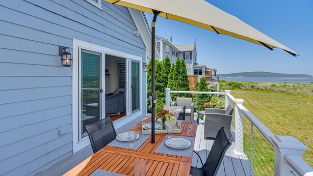 A deck with outdoor furniture, a table set with plates and glasses, and a large umbrella providing shade.