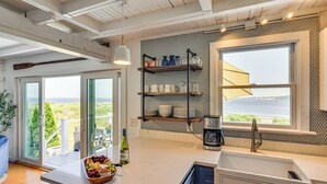 A modern kitchen with a large window, a built-in shelf with kitchenware, and a bowl of fruit on the counter.