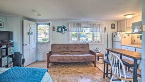 A cozy room with a sofa, a dining table with chairs, a kitchen area, and a door leading outside. - Romantic Cape Cod Studio w/ Patio, Near Beaches (Dennis Port)