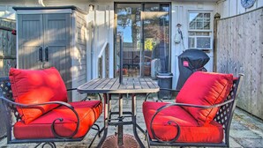 A patio with two red cushioned chairs and a small table, a covered grill, and a wooden fence. - Romantic Cape Cod Studio w/ Patio, Near Beaches (Dennis Port)