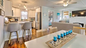 A modern kitchen with white cabinets, stainless steel appliances, and a dining area with a white table and bar stools. - Cozy Coastal Cottage: 5 Mi to Narragansett Beach! (Narragansett)