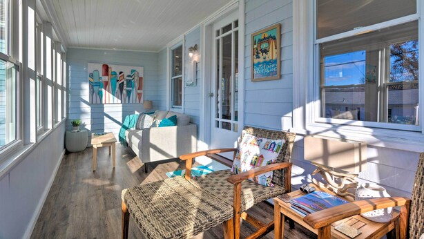 A cozy room with a wooden floor, a wicker chair, a small table, and a sofa with a blue cushion. - Cozy Coastal Cottage: 5 Mi to Narragansett Beach! (Narragansett)