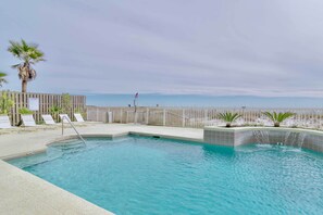 A pool area with a wooden fence, lounge chairs, and a view of the ocean. - Beachfront Gulf Shores Condo w/ Pool (Gulf Shores)