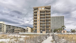 Un hôtel à plusieurs étages doté de balcons, une plage de sable et un ciel nuageux.