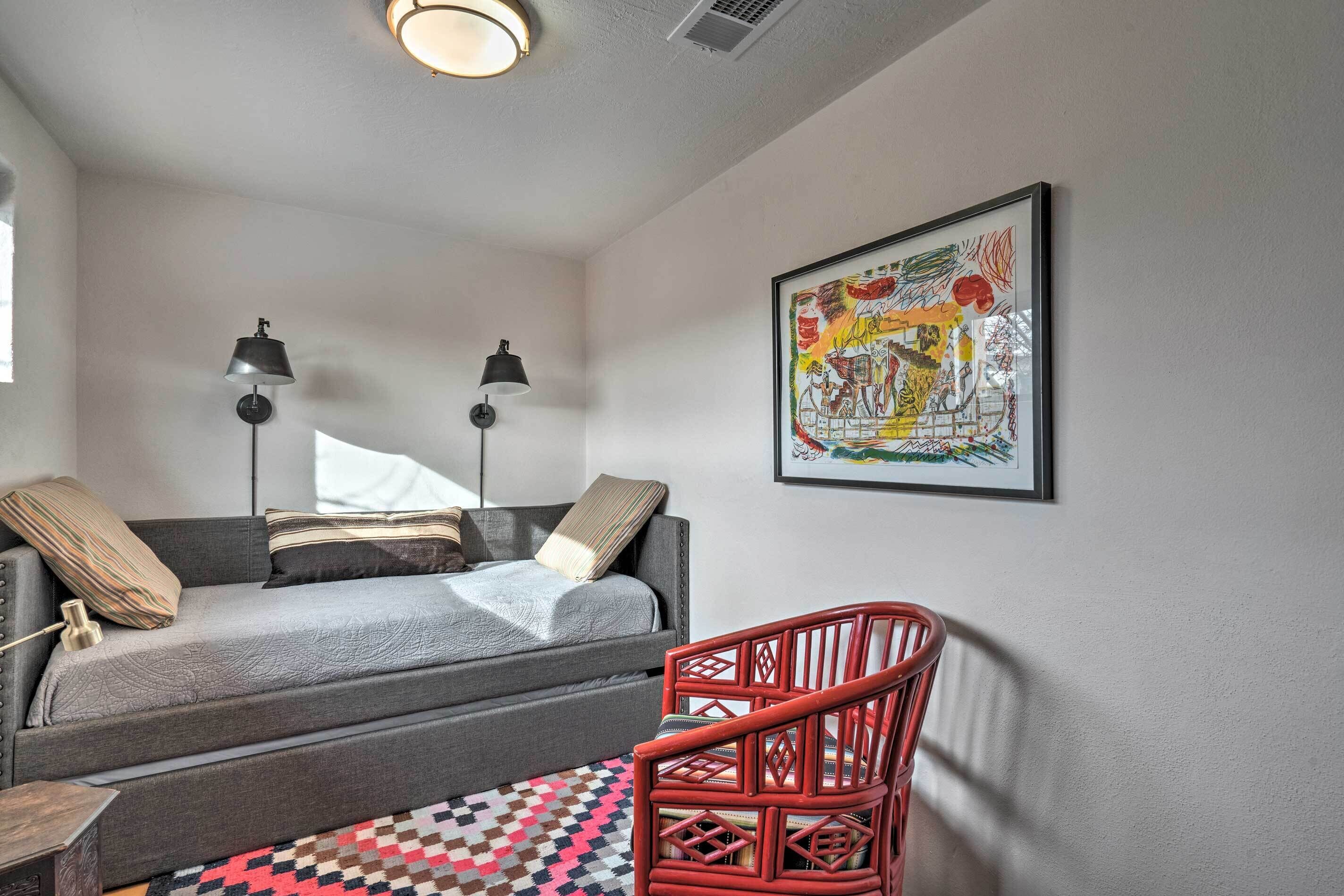 Une pièce chaleureuse avec un canapé gris, un fauteuil rouge, un tapis à motifs et un tableau abstrait encadré accroché au mur.
