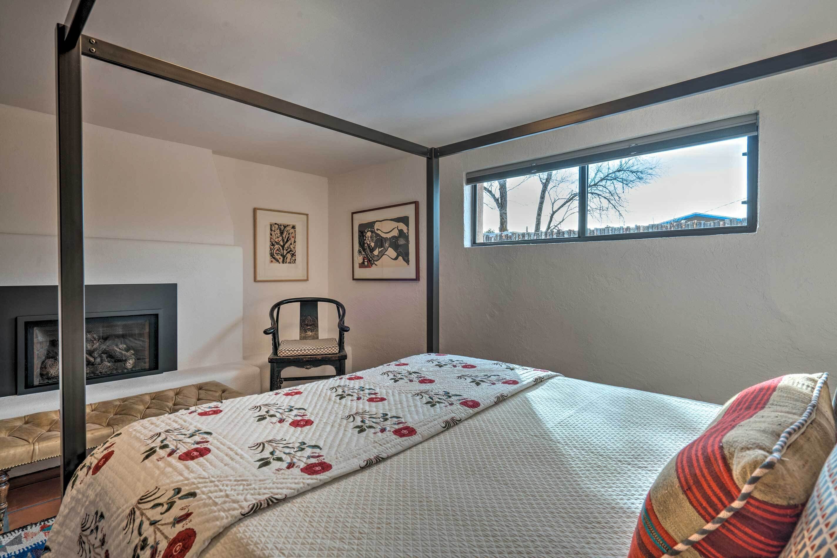 Une chambre à coucher avec un lit à baldaquin, une cheminée, une fenêtre donnant sur un beau paysage et deux tableaux encadrés accrochés au mur.