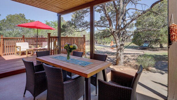Eine überdachte Terrasse mit Holztisch und Korbstühlen, einem roten Sonnenschirm und Blick auf Bäume und einen Zaun.