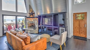 A spacious living area with a stone fireplace, large windows, and a high ceiling. - 10 Mi to Skiing: Tahoe City A-frame Home (Tahoe City)