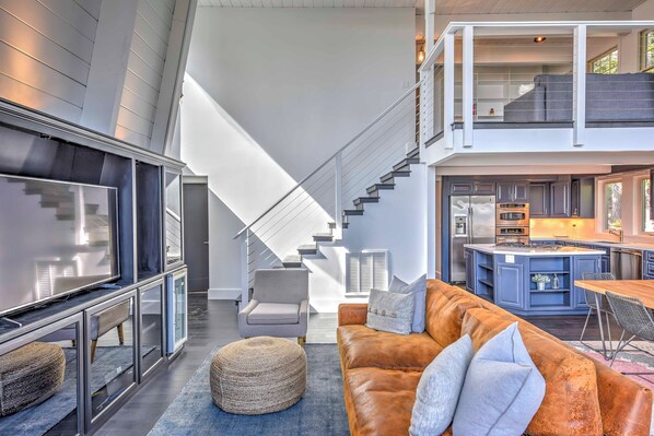 A modern interior with a staircase, a living area with a sofa and ottoman, and a kitchen area.