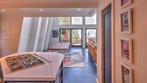 A modern kitchen with a gas stove, dining table, and chairs. There is a large window with blinds, a door leading to a balcony, and artwork on the walls. - 10 Mi to Skiing: Tahoe City A-frame Home (Tahoe City)