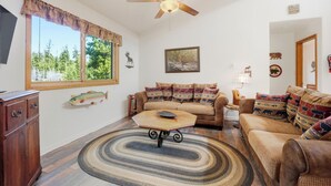 A cozy living room with a ceiling fan, a sofa set, a coffee table, and a large window with a view of trees. - Large Home on 1 Acre: 2 Mi to Grand Lake Village (Grand Lake)