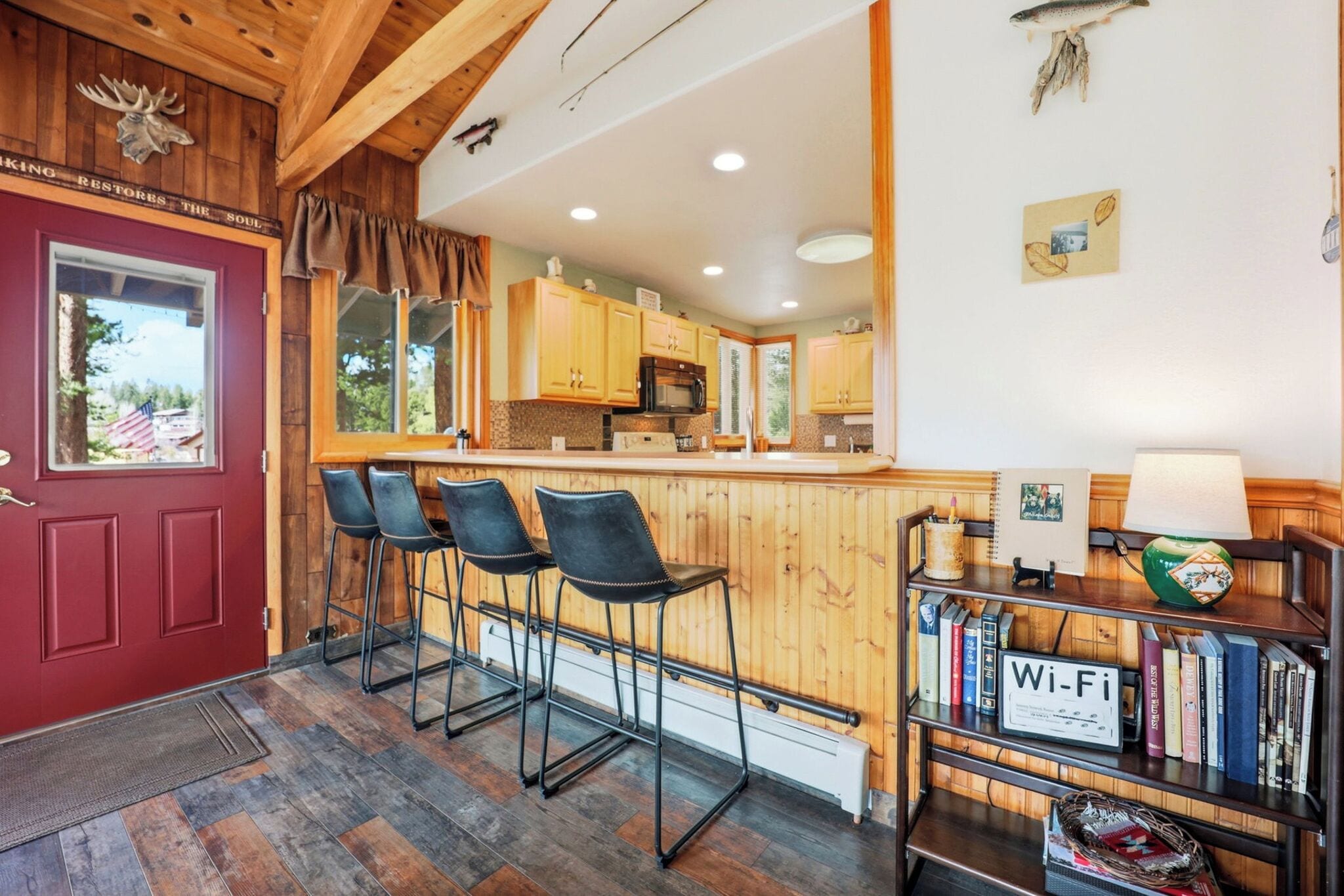 A cozy kitchen with wooden cabinets, a bar area with stools, and a bookshelf with books and a Wi-Fi sign.