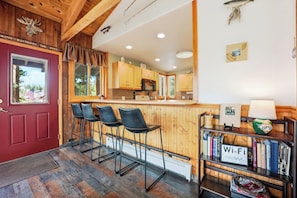 Une cuisine chaleureuse avec des meubles en bois, un coin bar avec des tabourets et une bibliothèque remplie de livres, ainsi qu’un panneau indiquant la présence d’une connexion Wi-Fi.