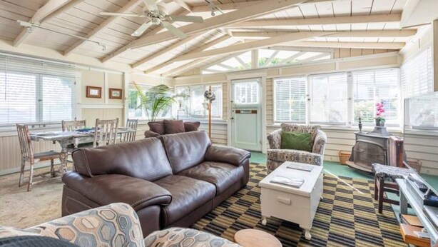 Un salón amplio con un sofá de cuero marrón, un sillón estampado y una mesa de centro blanca. Hay una zona de comedor con una mesa y sillas, y un televisor sobre un mueble de madera.