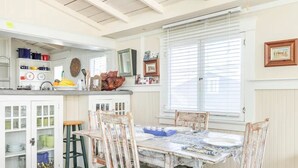Un comedor con mesa y sillas, una zona de cocina con armarios y utensilios, y una ventana con persianas.