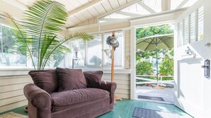 Una habitación acogedora con un sofá de mimbre, una planta grande y vistas al exterior a través de un ventanal corredero.