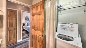 A laundry area with a washing machine, wooden doors, and a bed in the background. - Buena Vista Condo: 1/2 Mile to River & Main St! (Buena Vista)