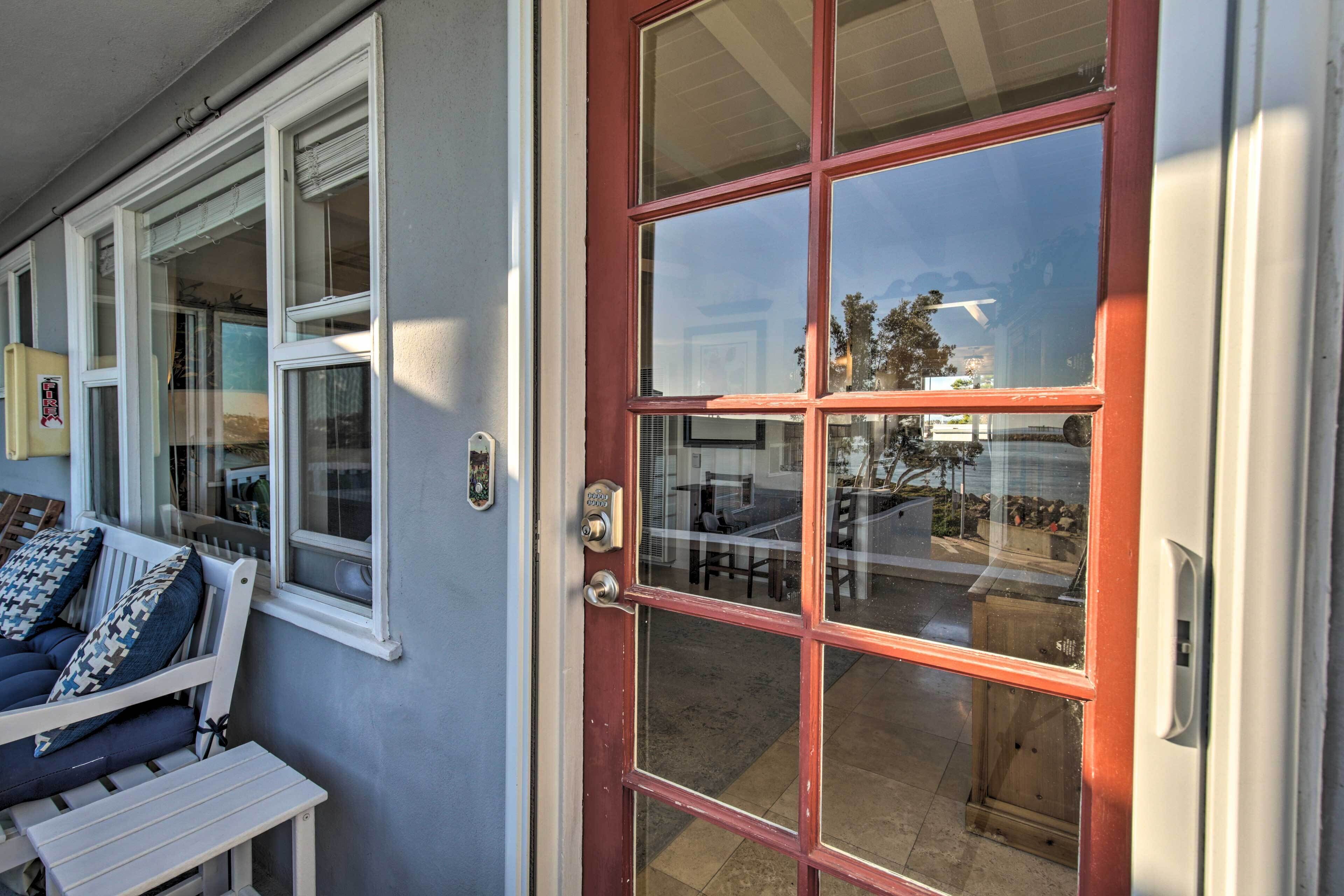 A front door with a red frame, a white bench with cushions, and a window with a view of the outside.