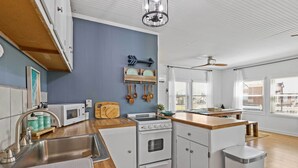 A compact kitchen with a microwave, stove, sink, and wooden countertop.