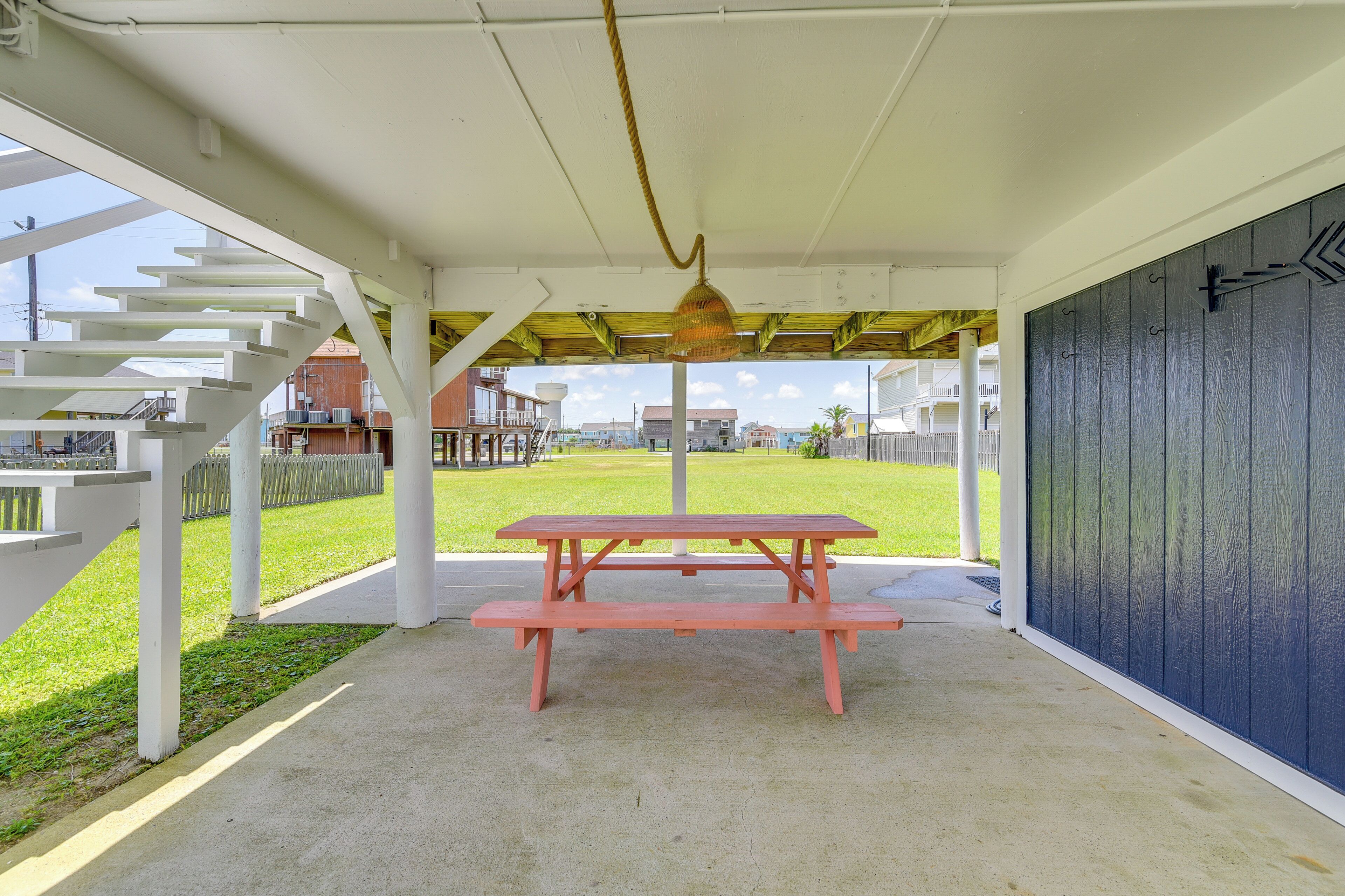 A covered picnic area with a table and benches, a white staircase, and a view of a grassy area and buildings in the background.