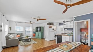 A spacious living area with a wooden dining table, a gray sofa, and a kitchen in the background.