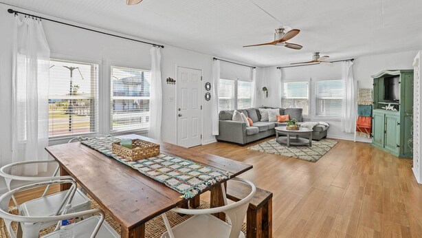 A spacious living room with a wooden dining table, white chairs, a gray sofa, and a green cabinet.