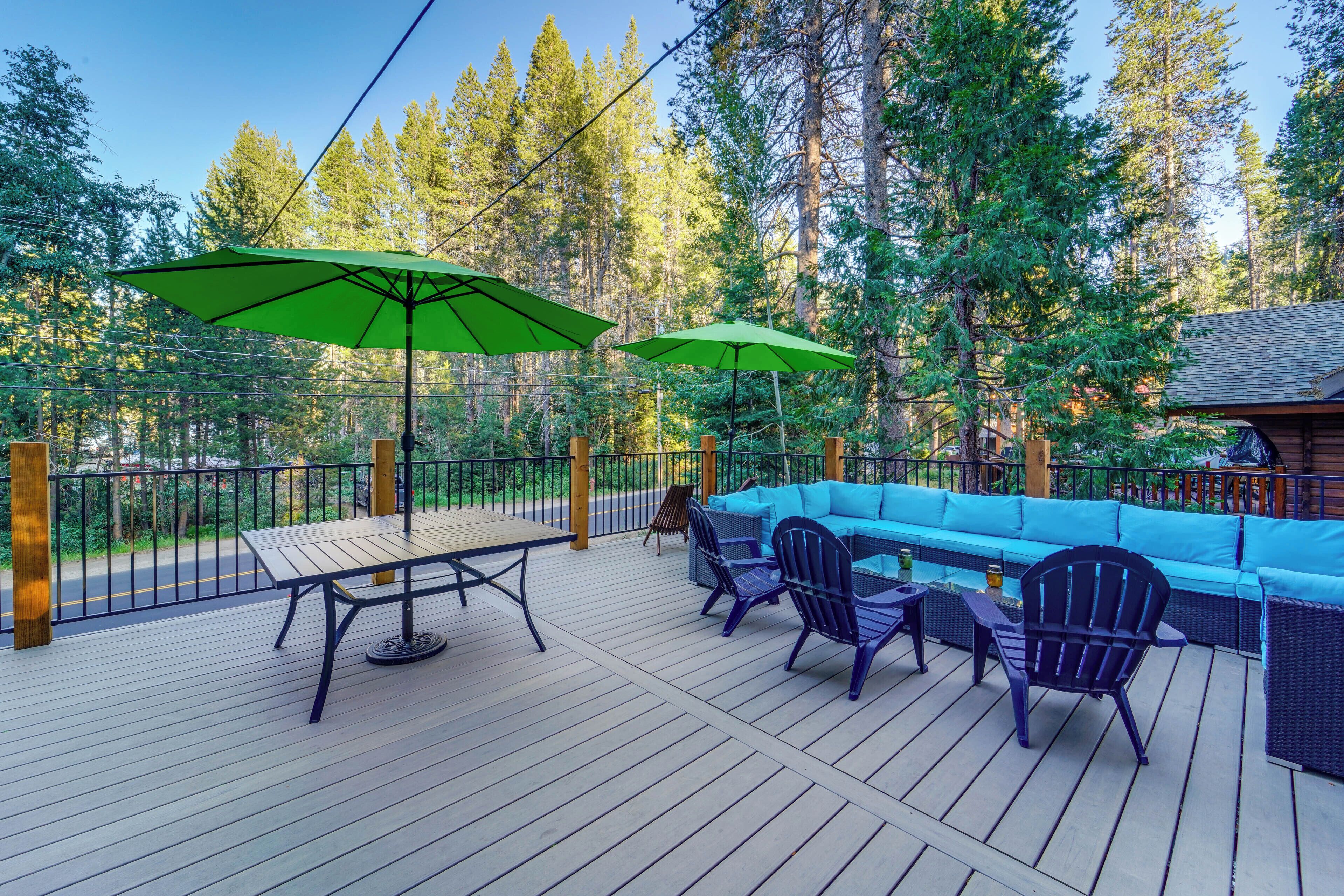 A wooden deck with a blue sofa and chairs, two green umbrellas, and a table.
