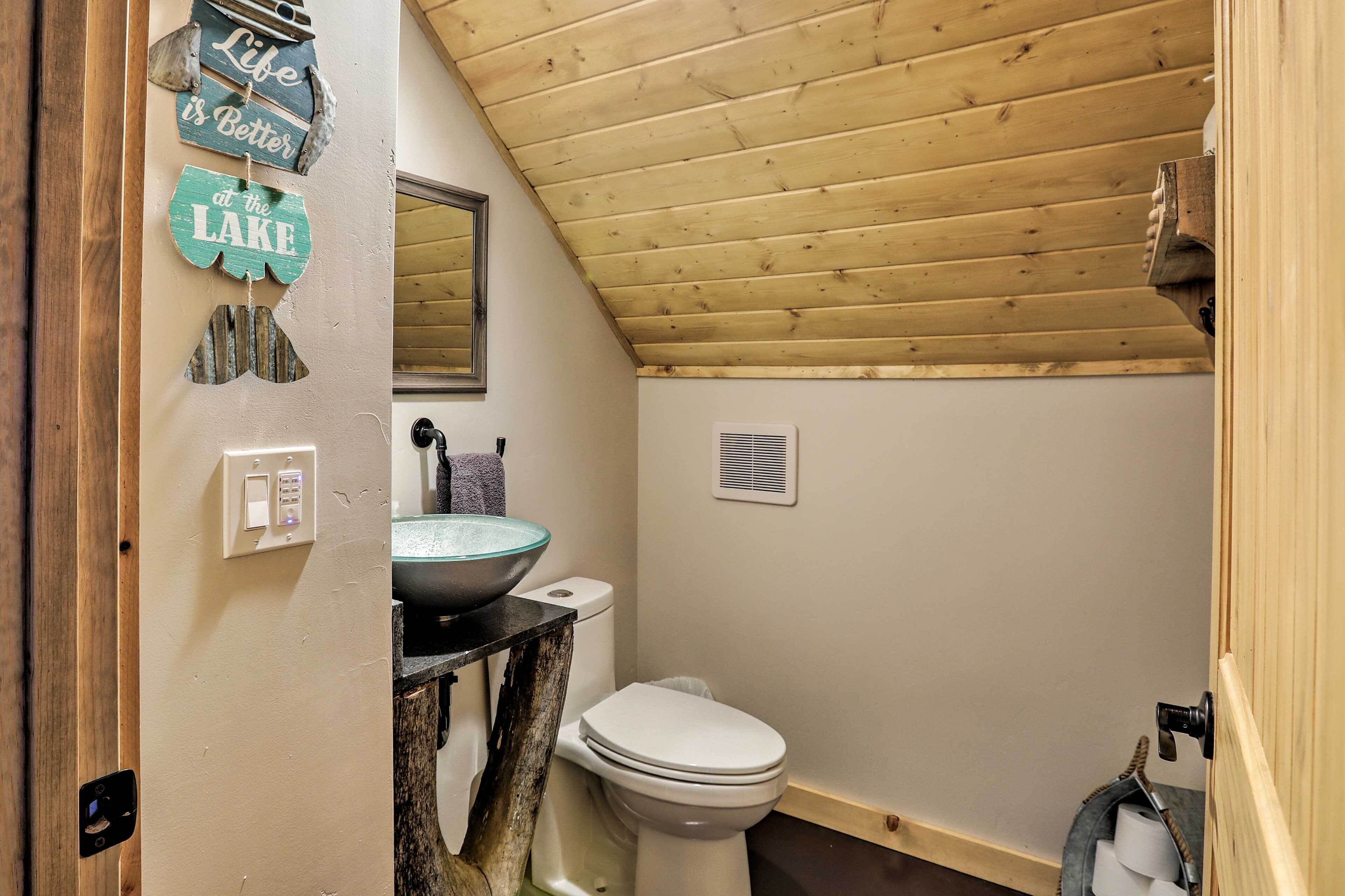 A small bathroom with a wooden ceiling, a toilet, a sink with a glass basin, and a towel hanging on the wall.