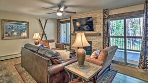 A living room with a stone fireplace, leather sofas, a television, and a ceiling fan. - Breck Ski-in/ski-out Condo on Peak 8 w/ Patio (Breckenridge)
