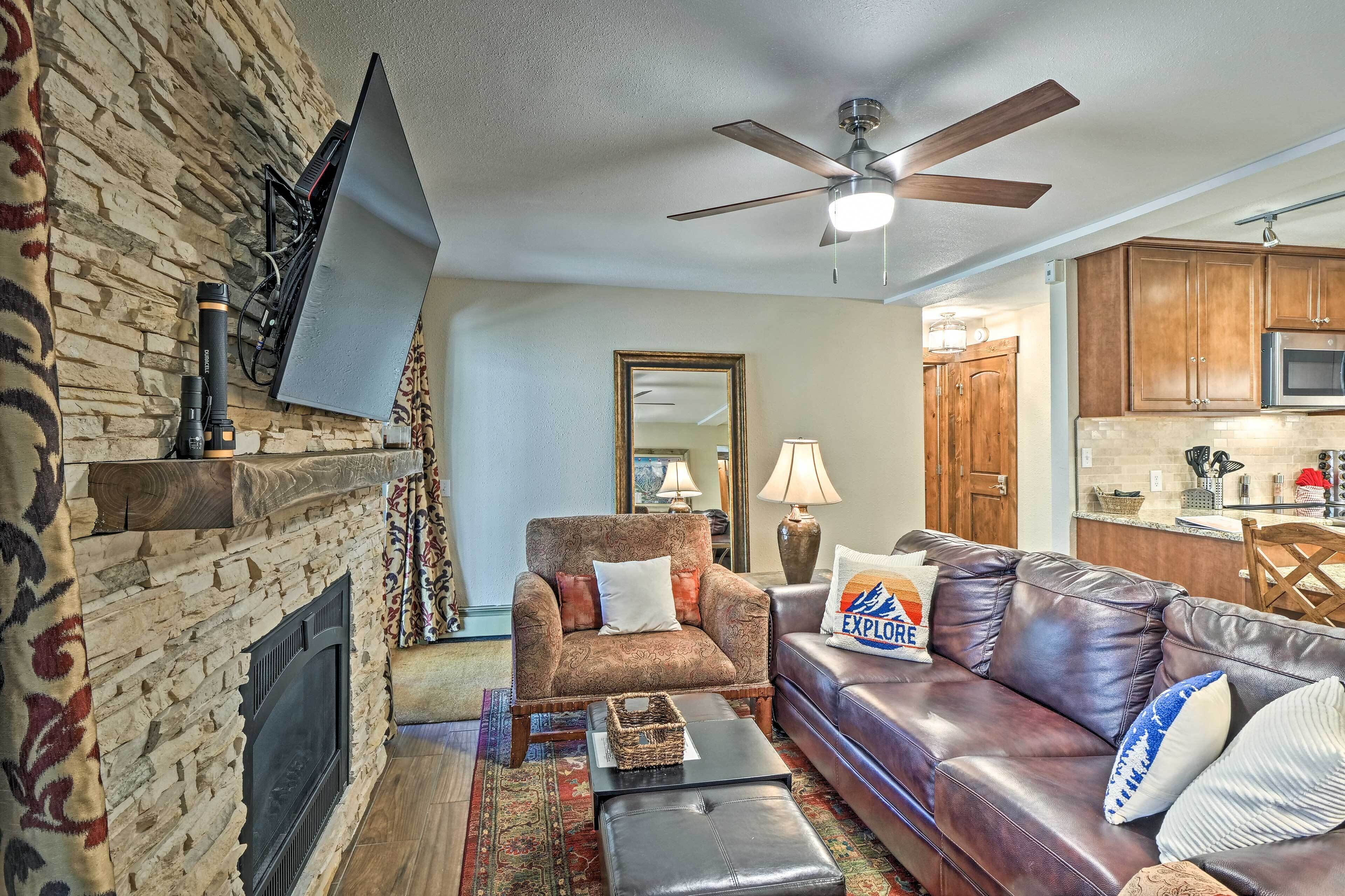 A living room with a stone fireplace, leather sofa, and a flat-screen TV mounted on the wall.