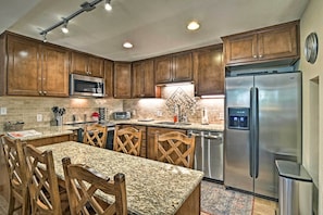 A kitchen with granite countertops, wooden chairs, a stainless steel refrigerator, and a microwave. - Breck Ski-in/ski-out Condo on Peak 8 w/ Patio (Breckenridge)
