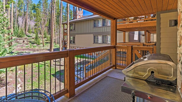 A covered outdoor area with a grill, wooden deck, and a view of a house and forest. - Breck Ski-in/ski-out Condo on Peak 8 w/ Patio (Breckenridge)