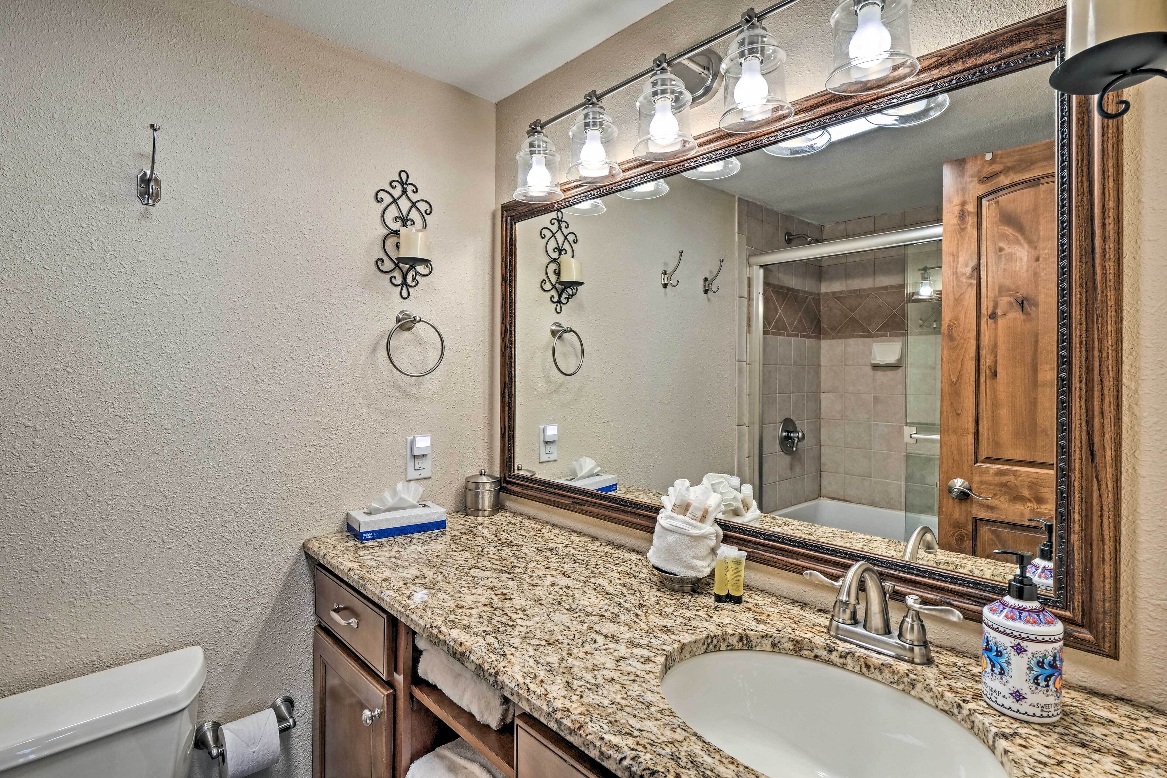 A bathroom with a granite countertop, a sink, a mirror, and a toilet.