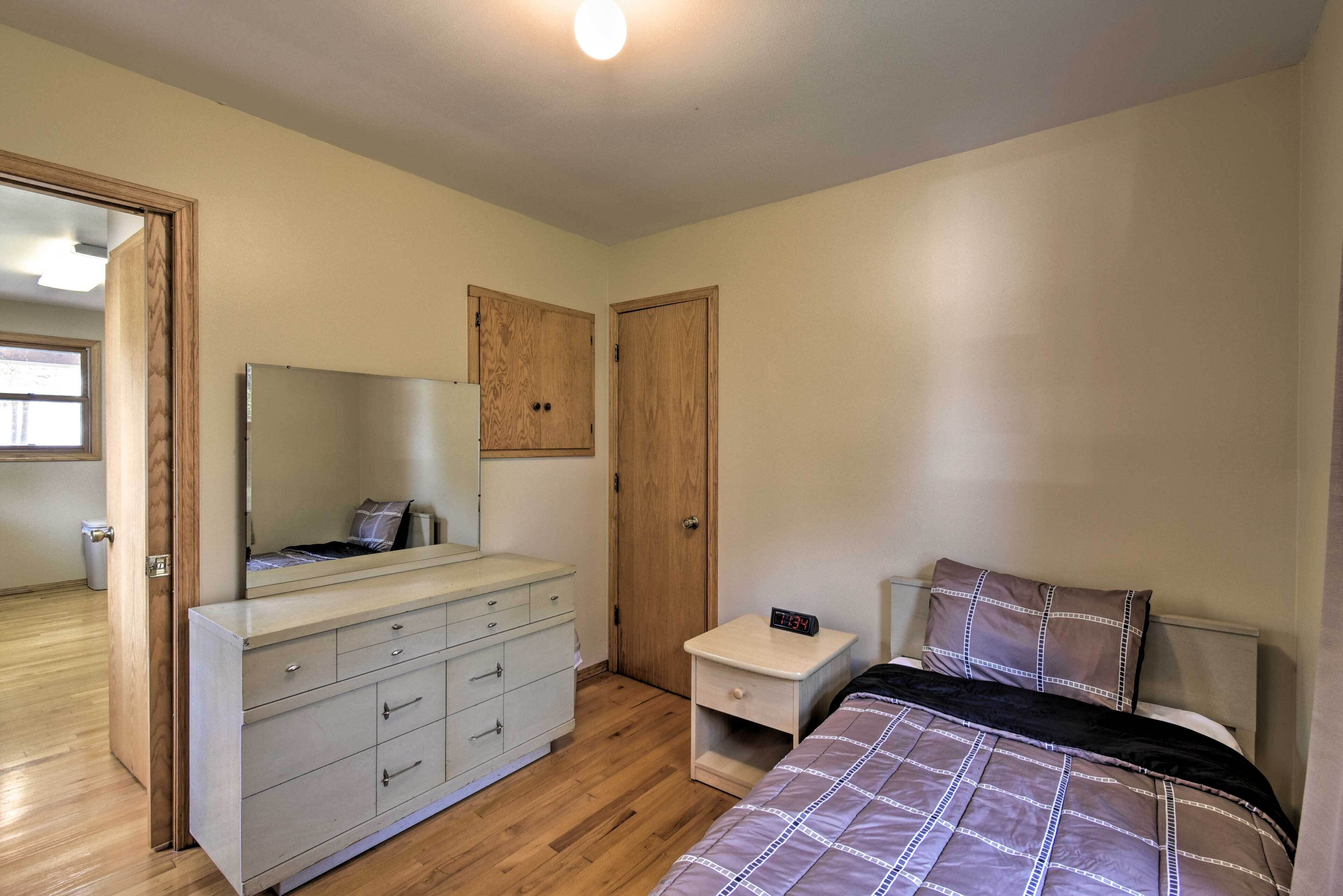 A bedroom with a bed, a dresser, a nightstand, a mirror, and two doors.